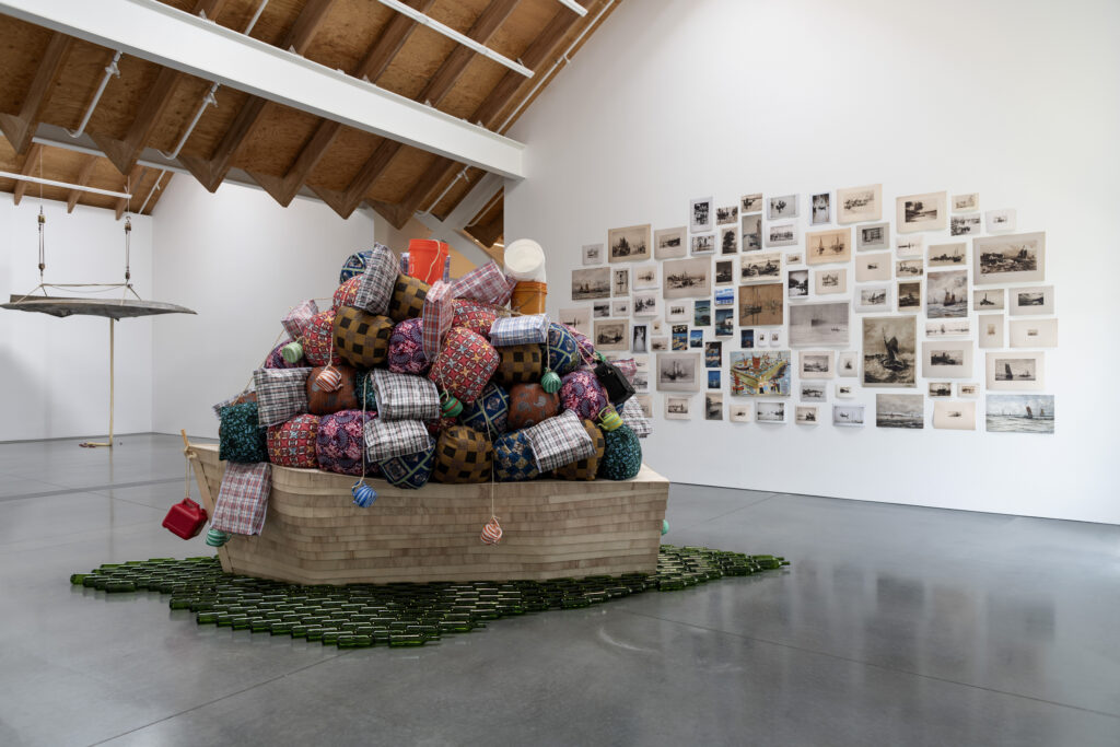 Barthélémy Toguo b. 1967, Cameroon Road to Exile, 2018 Wooden boat, cloth bundles, glass bottles, and plastic containers 120 × 60 × 45 inches
